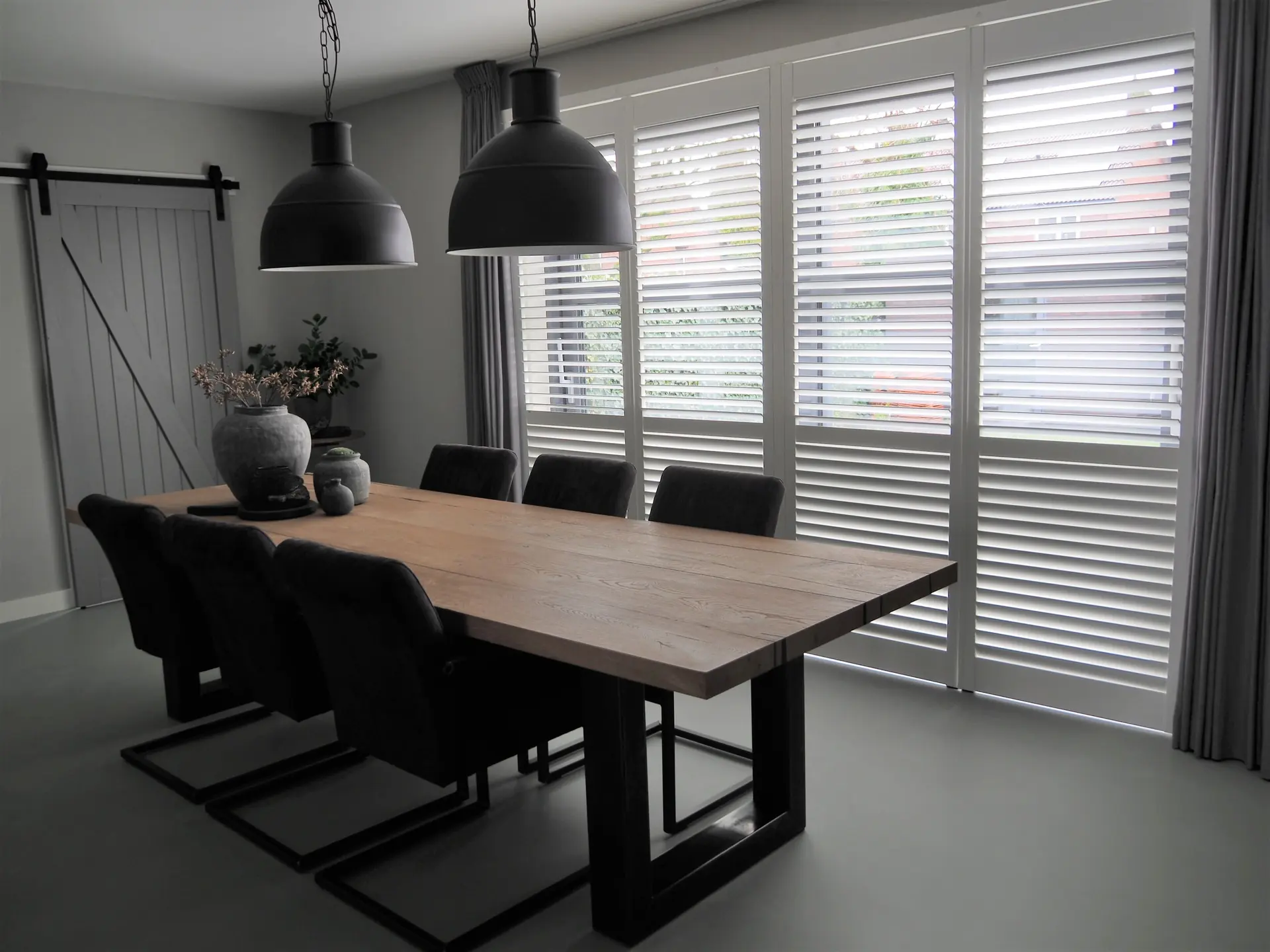 Eethoek met eiken tafel, zwarte hanglampen en shutters voor de schuifpui