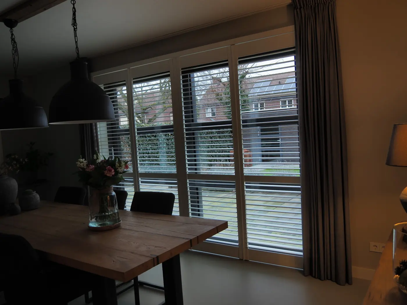 Jaloezieën in een eethoek met eiken tafel en zwarte hanglampen