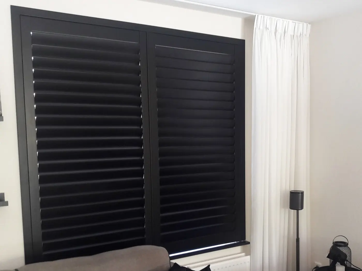 Antracietkleurige shutters voor een woonkamerraam, met witte vitrage ervoor