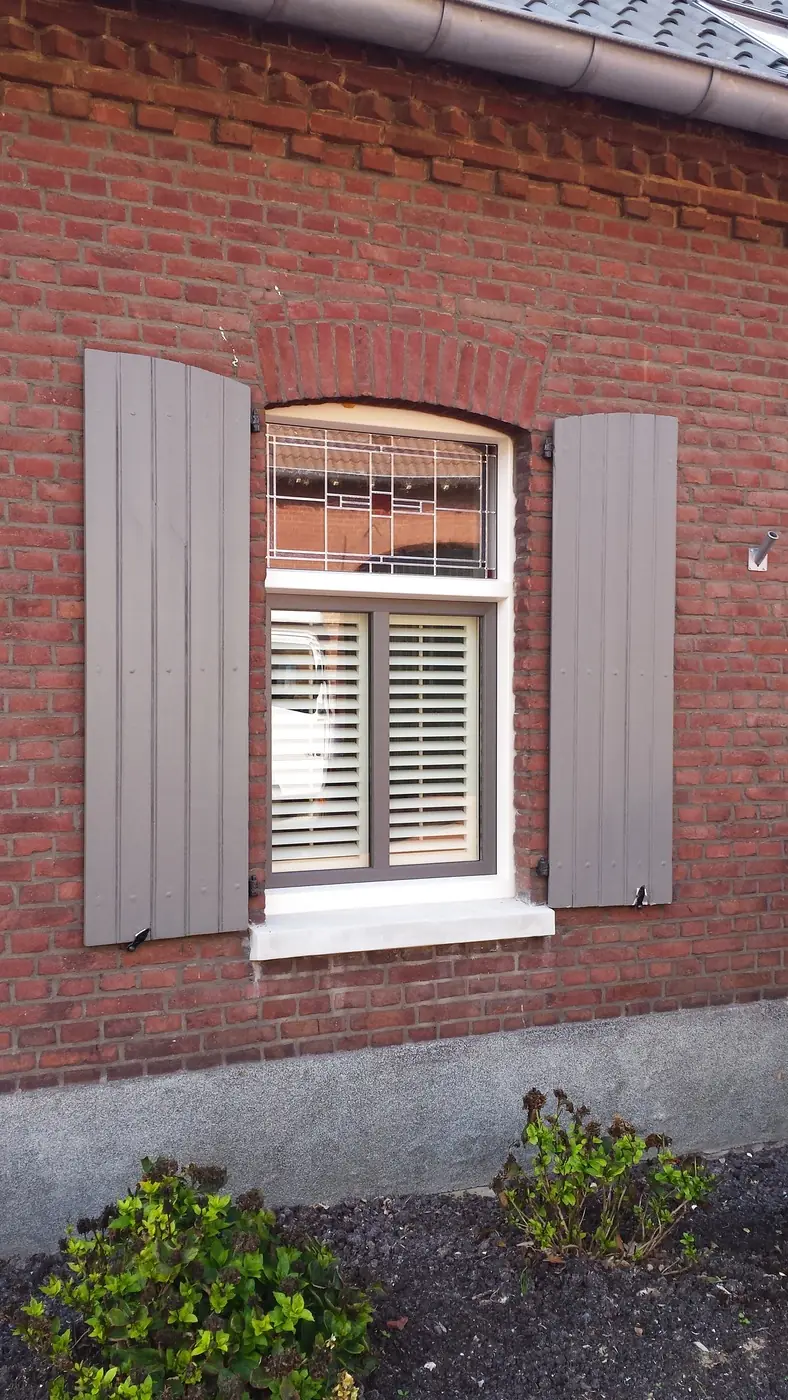 Shutters achter een boogvenster in een bakstenen gevel, met luiken ernaast