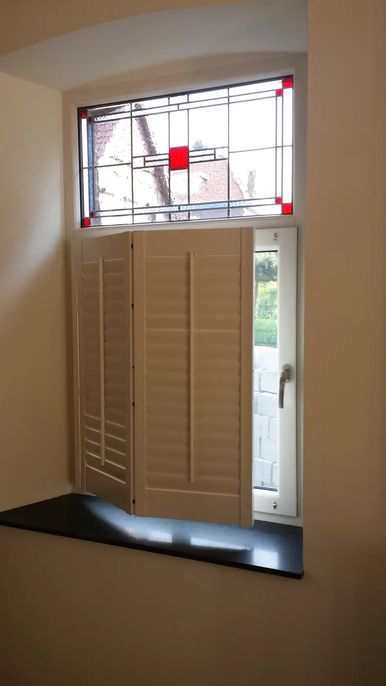 Shutters onder een schuin dakvlak, naast een glas-in-loodraam