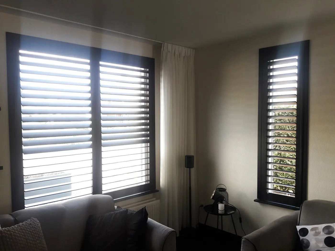 Witte shutters en vitrage in een woonkamer, lamellen half geopend